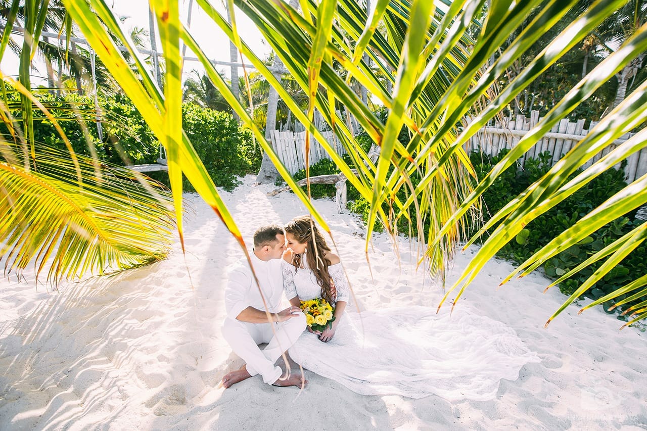 жених и невеста сидят на песке на пляже под пальмой