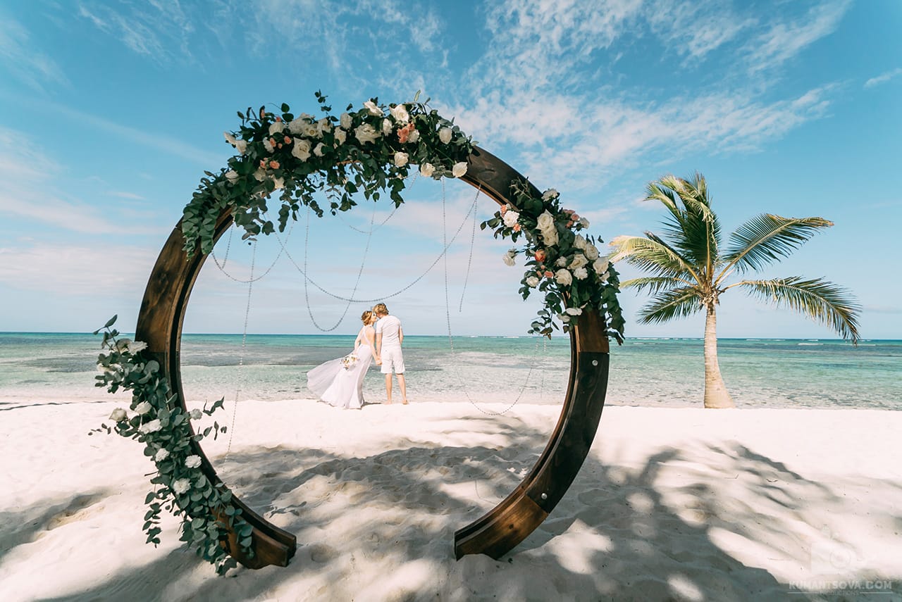 жених и невеста в свадебной арке возле пальмы на пляже