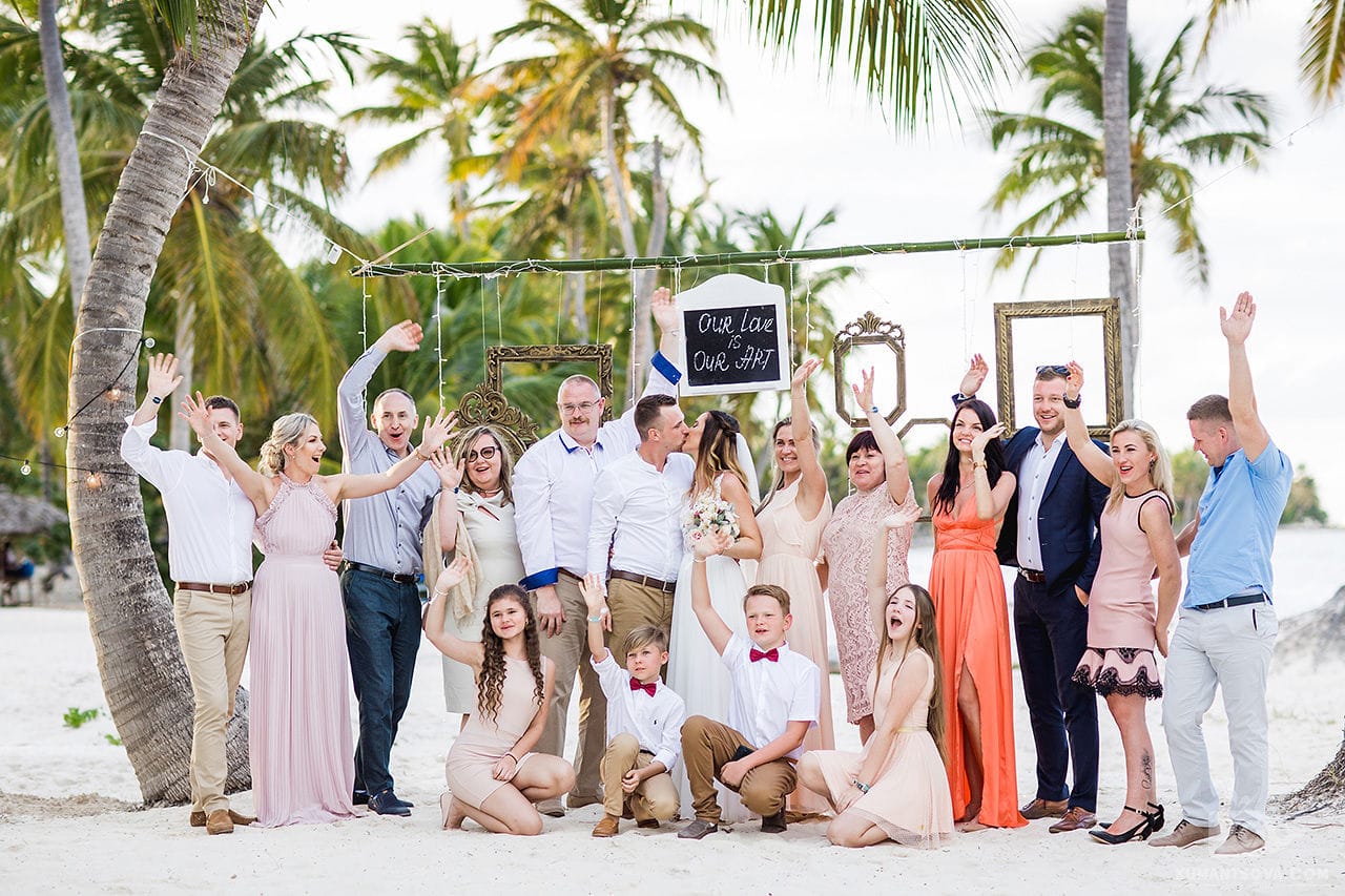 гости со свадьбы с женихом и невестой под пальмой